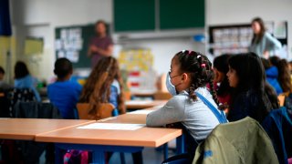 A girl wears a face mask as students sit in a classroom o