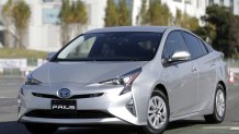 A silver Toyota Prius with two passengers inside during the day.