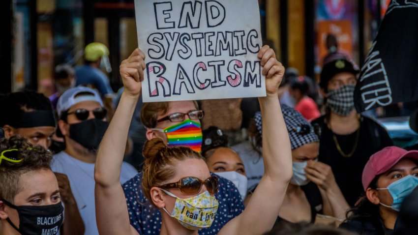 Una participante de una protesta contra el abuso policial muestra un cartel que dice Fin del racismo sistémico en la protesta.