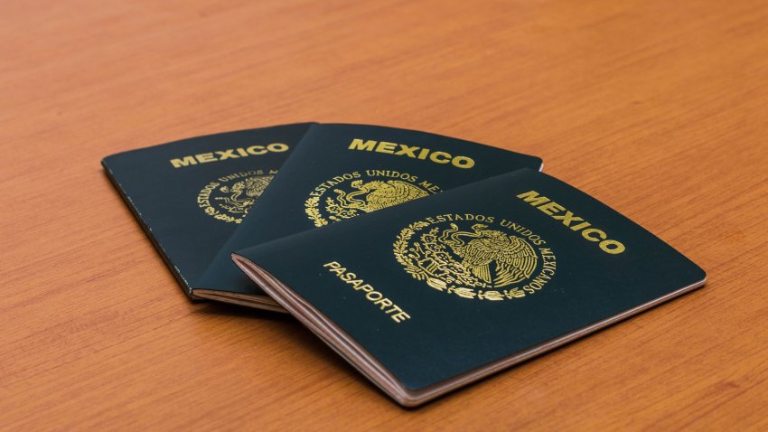 Tres pasaportes mexicanos apilados en la mesa de madera en el fondo. Vista lateral. La portada de un pasaporte mexicano. Concepto de turismo y viajes