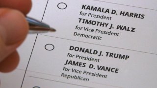 Una mano se sitúa entre la votación por Kamala Harris y Tim Walz o por Donald Trump y JD Vance en una representación de una boleta impresa para la elección presidencial.